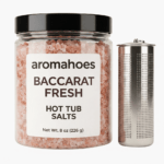 A transparent 8oz jar labeled "aromahoes BACCARAT FRESH Hot Tub Salts" filled with pink himalayan crystals next to a perforated stainless steel port canister dispenser. White background.
