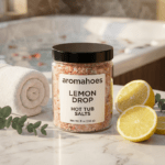 Aromahoes Lemon Drop Hot Tub Salts on a marble surface with fresh lemon slices and a rolled white towel, hot tub in the background.